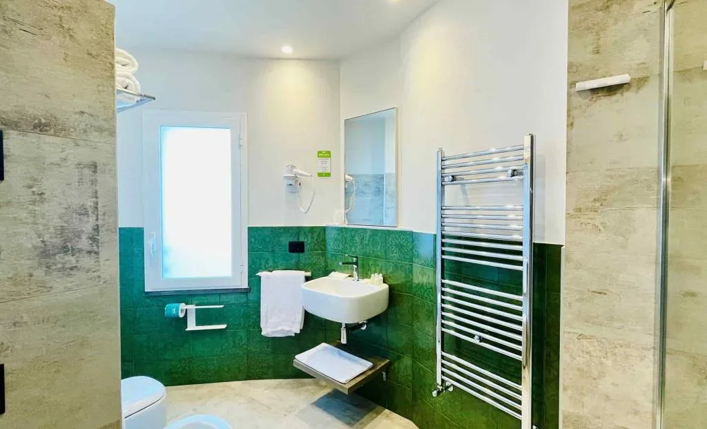 Bagno luminoso con finestra, lavabo e pareti in piastrelle verdi