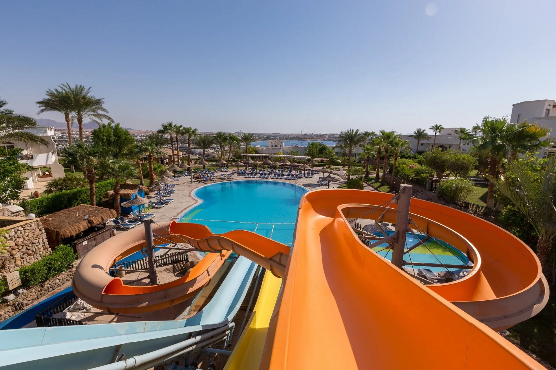 Vista dall'alto degli scivoli acquatici con piscina, palme e mare sullo sfondo
