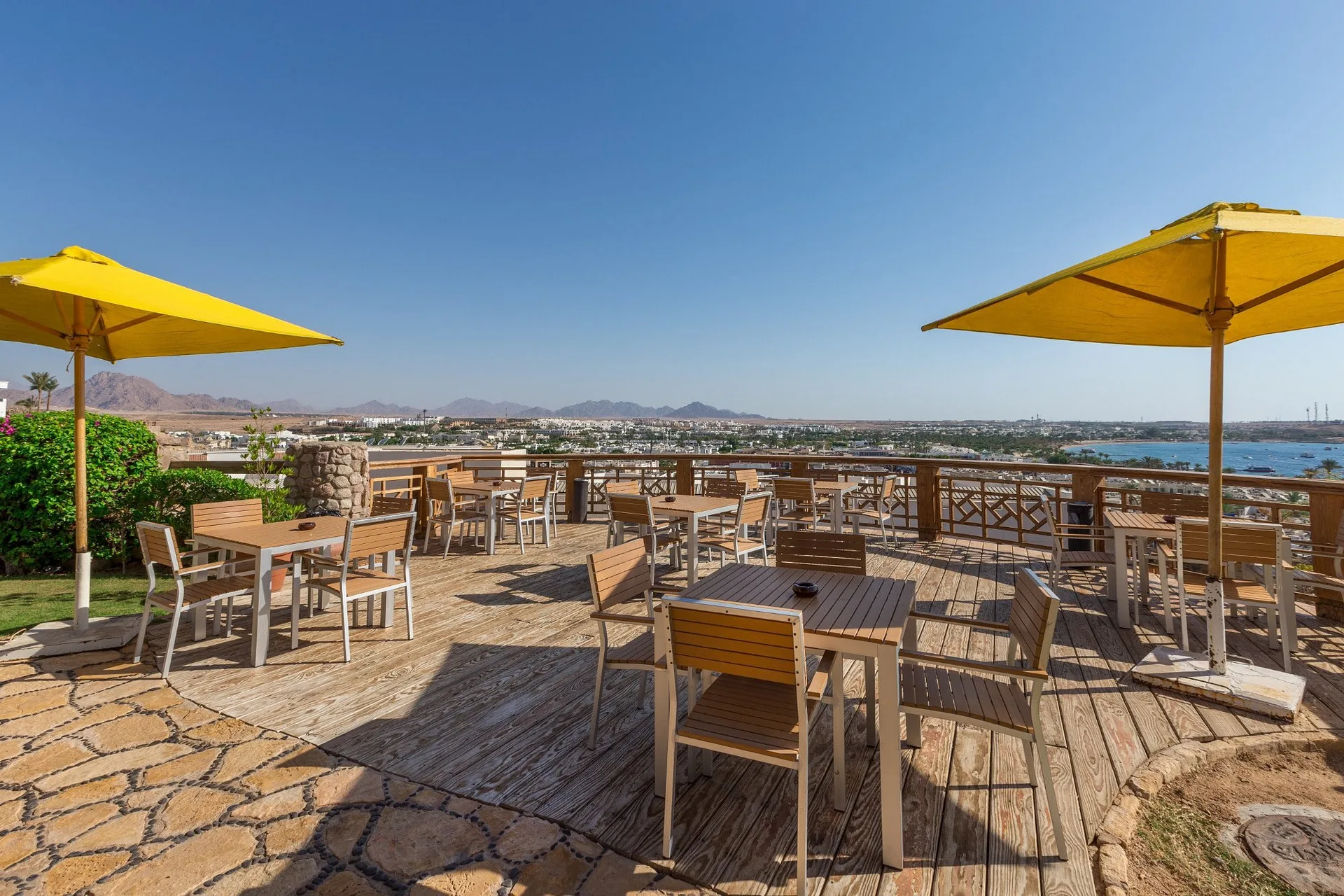 Terrazza ristorante con tavoli in legno, ombrelloni gialli e vista panoramica sulla città