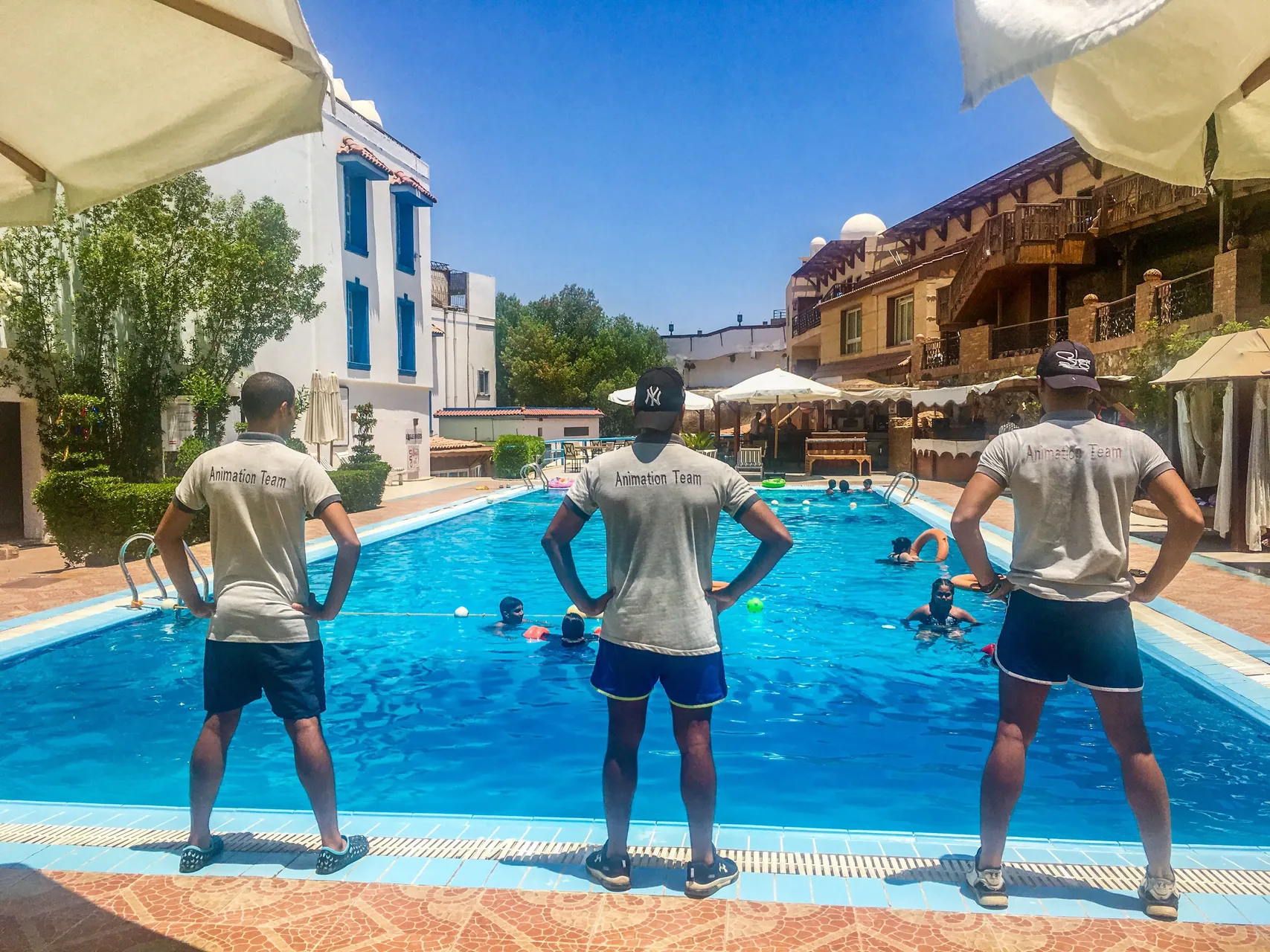 Team di animazione di spalle a bordo piscina mentre gli ospiti nuotano