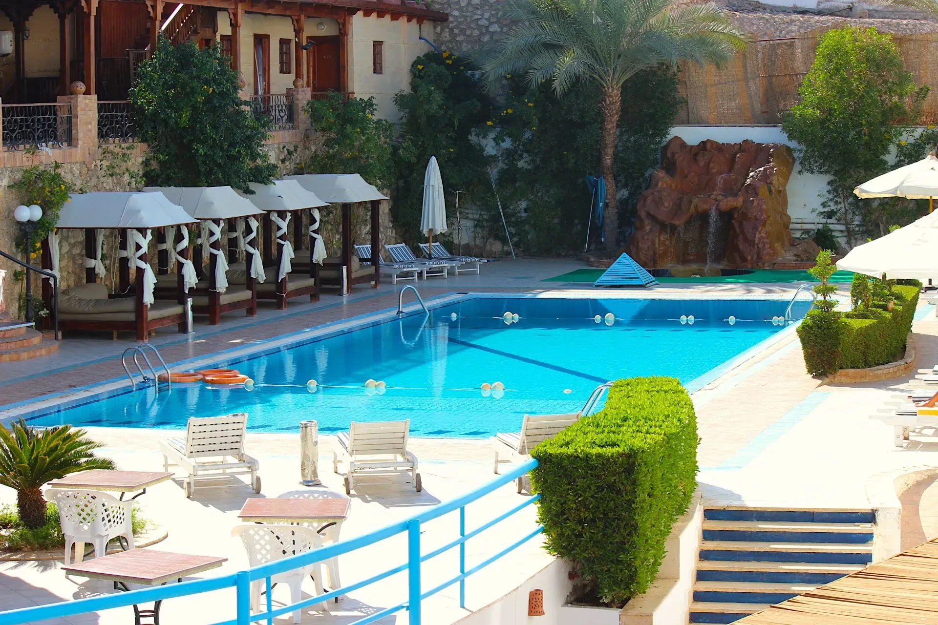 Piscina con lettini, gazebi e cascata rocciosa in ambiente curato con vegetazione
