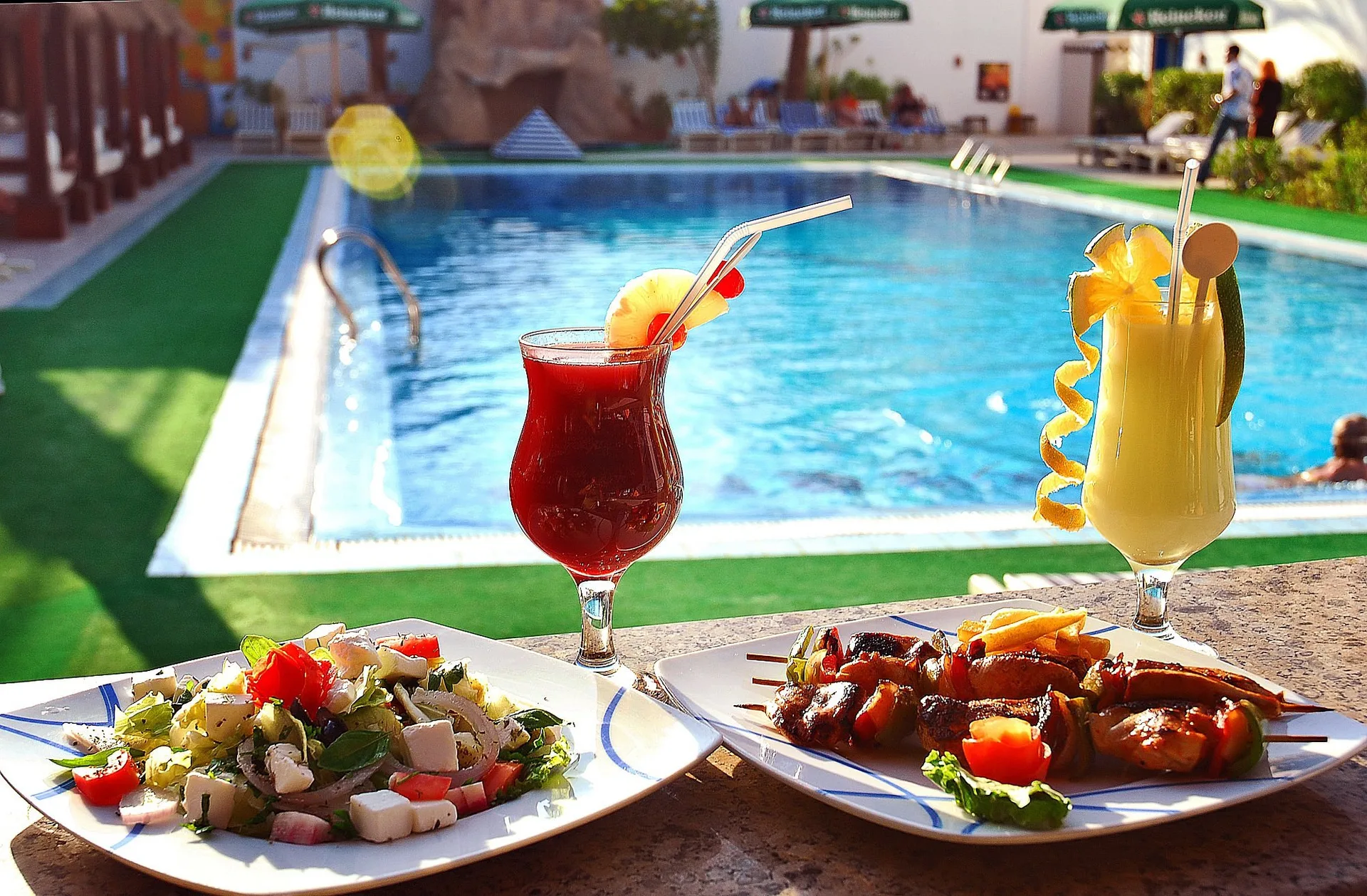 Piatti di insalata e carne grigliata con cocktail colorati a bordo piscina