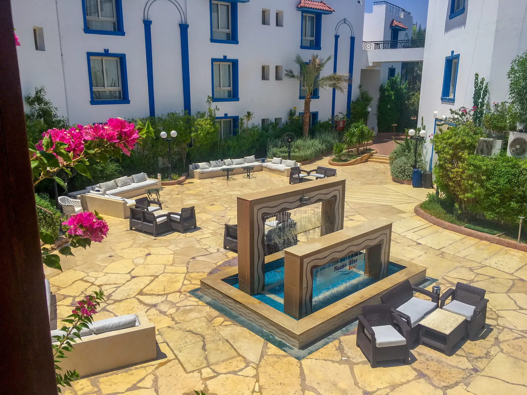 Terrazza interna in pietra con fontana, divani e poltrone circondata da edifici bianco e blu