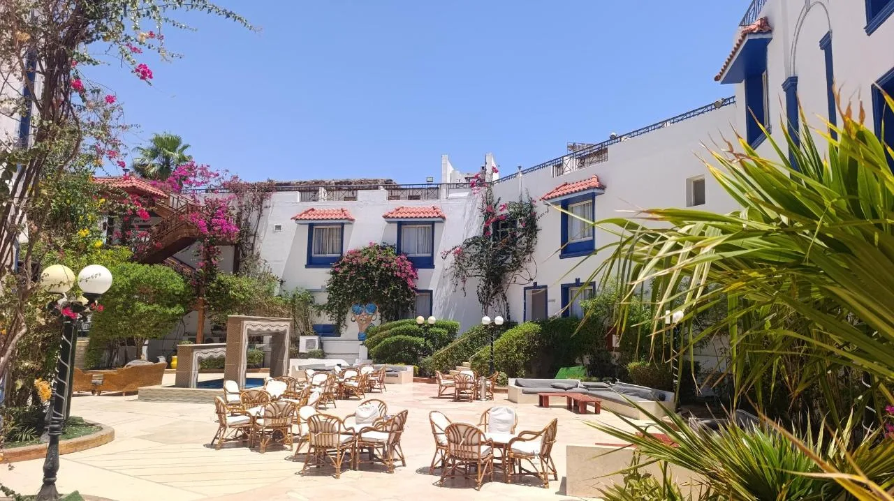 Cortile interno con tavoli e sedie in rattan, edifici bianchi e fiori bougainvillea rosa